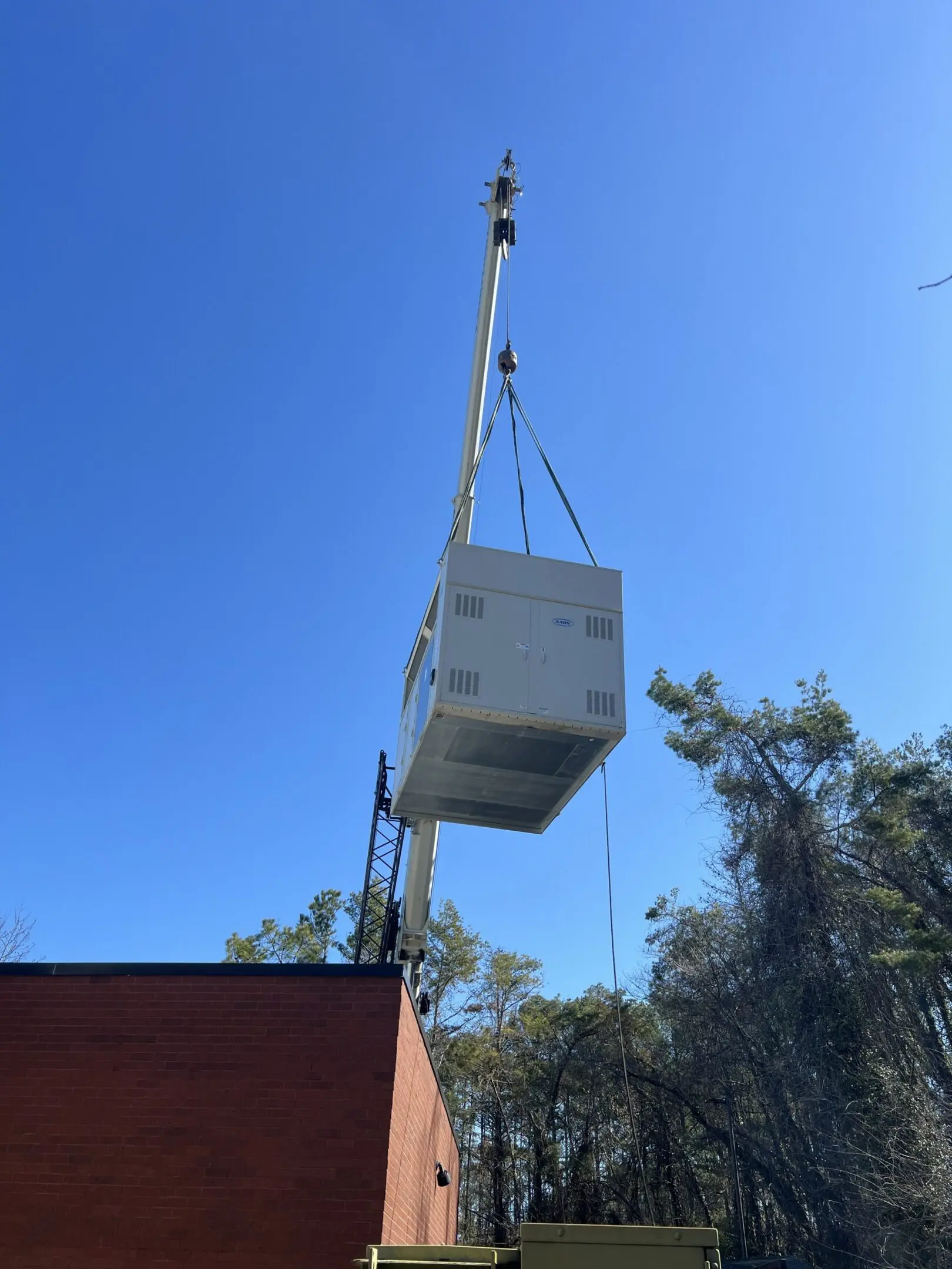 Crane lifting white modular unit over building